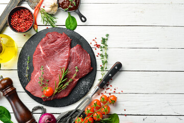 Two pieces of fresh raw veal with rosemary and spices. On a white wooden background. Top view.