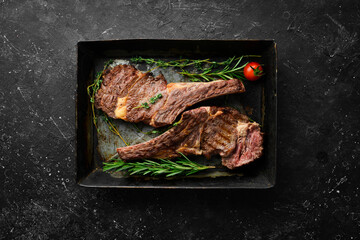 Two veal steaks on the bone with spices, thyme and rosemary. Barbecue meat. Top view. Flat lay top view on black stone cutting table.