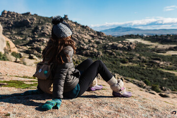 Young active woman with trekking equipment sitting, relaxing and looking at lake and mountains background