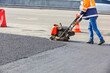 A road worker compacts asphalt with a petrol vibratory plate compactor.