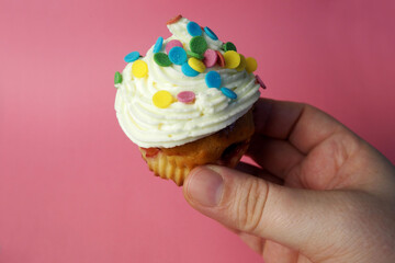 in the right hand they hold a diet yogurt muffin with red currant smeared with white cream and mascarpone decorated with colorful round splashes on a pink background side view . homemade cakes