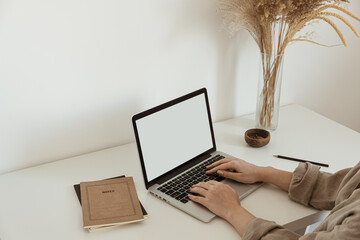 Office desk workspace with girl's, women's hands typing on laptop. Laptop computer with blank copy space display screen, notebook, reeds pampas grass bouquet.