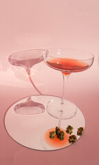 Red wine glass with rose red wine, and a cannabis dry leafs on a mirror, on a pink background. Artsy women cannabis concept.