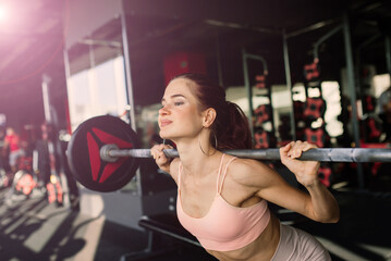 A young and beautiful female trains with a barbell in the gym. Posing with elements for training