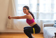 © Leo Cerz - Healthy and attractive young woman is exercising in her living room. She wears black leggins, a pink top, and a green league