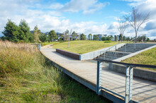 Pedestrian Boardwalk Footpath In A Suburban Park Leads To A Neighborhood With Some Modern Australian Houses In The Distance. Concept Of The Public Green Land In The Suburb And The Local Park.