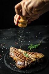 Wall Mural - Grilled Porterhouse steak on a black plate by chef in the kitchen. Gourmet t-bone steak cooked on grill in American meat restaurant.