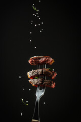 Traditional American barbecue dry aged flank steak sliced on a fork adding rosemary and sea salt in a freeze motion on black background. vertical image, American cuisine