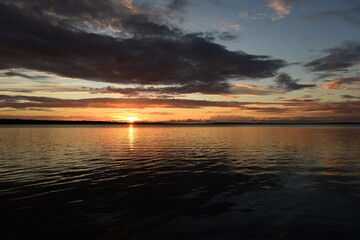 Wall Mural - Sunbeam in the sky from under a dark cloud of the setting sun on the horizon above the water on sunset