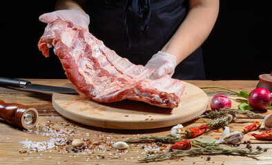 Wall Mural - The chef uses his hands to slice pork ribs with a knife on a wooden cutting table. Selective focus. The concept of the cooking process.