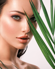 Wall Mural - Young beautiful woman with green leaves near face. Skin care beauty treatments concept.  Closeup girl's face with green leave.