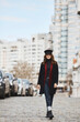 Outdoor spring portrait of young elegant fashionable woman wearing trendy sunglasses, red coat and hat walking in a street of European city
