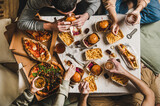 Fototapeta Uliczki - Lockdown fast food dinner from delivery service. Flat-lay of friends sitting and having beer quarantine party with burgers, french fries, sandwiches, pizza and salad over table background, top view
