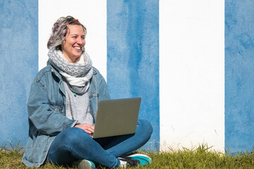 Sticker - Young Caucasian female sitting against a blue and white wall working on the laptop