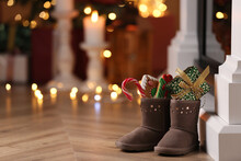 Boots Filled With Sweets And Gift On Floor In Room, Space For Text. Saint Nicholas Day