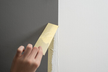 hand taking off masking tape from the wall after painting