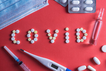 The inscription Covid, made of white round tablets. Disposable syringe and vial drug on a red background. COVID-19 coronavirus vaccine.