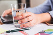 © René Stevens - Close-up of a businesswoman using her laptop at the office desk, with a glass of water.