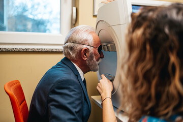 Wall Mural - Elegant senior bearded man receiving ophthalmology treatment. Doctor ophthalmologist checking his eyesight with modern equipment.