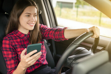 Wall Mural - Young smiling woman in casual dress with phone driving modern car