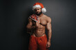 © Serge Lee - Sad Santa Claus with red plaid in studio. Sexy muscular guy in Santa hat at grey background. Shirtless man in Christmas pants holding  checkered blanket on his chest.