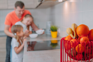 Wall Mural - A father feeds his daughters in the kitchen on a background of fruits.