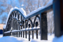A Snow-covered Black Forged Fence Made Of Thick Metal Profiles Is Positioned Diagonally In The Frame. Sunny Frosty Day In The Park. Selective Focus.