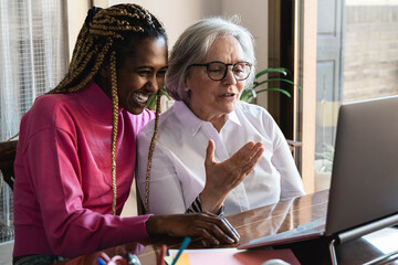 Multiracial senior and young woman having video call on on laptop computer at home during coronavirus lockdown - Elderly and technology - Focus on african girl