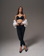 © Dmitry Tsvetkov - Full length studio portrait of young slim tanned caucasian girl in black jeans, bra and white jeans jacket standing and posing against grey studio background