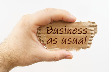 A man holds a cardboard in his hand on which it is written - Business as usual