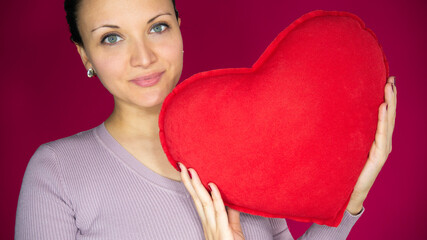 Portrait of a woman holding a red heart-shaped pillow on the red background. Celebrating  love.