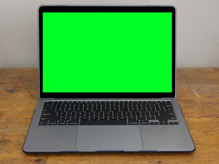 a modern laptop computer is shown isolated on an old, wood office desk, with a green screen on the m