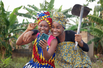 two amazed african nigerian female farmers joyfully staring at a smart phone