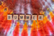 Bummer Spelled Out In Wooden Letters On A Hippie-style Burst Pattern Tie Dye Textile Background. February 2021. 