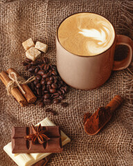 cup of coffee with cinnamon,  anise, coffee bean, chocolates   and sugar  on a wooden background