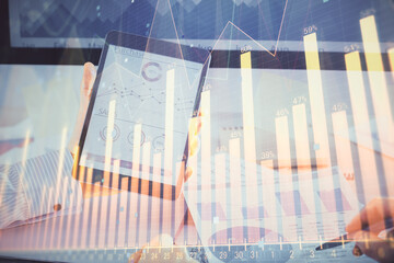 Double exposure of man's hands holding and using a digital device and forex graph drawing. Financial market concept.