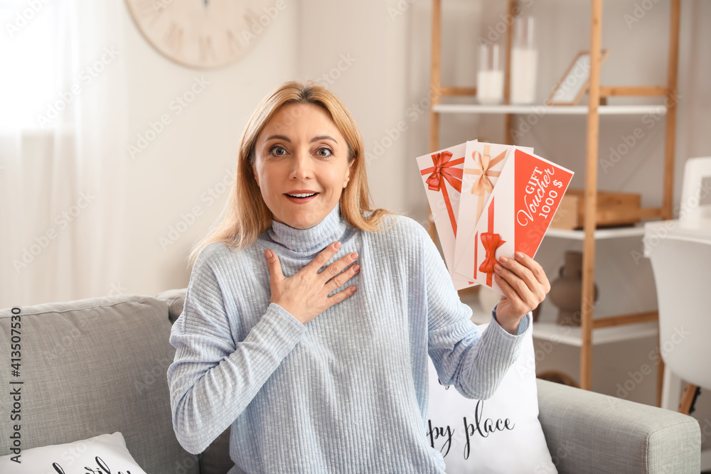 Surprised mature woman with gift cards at home