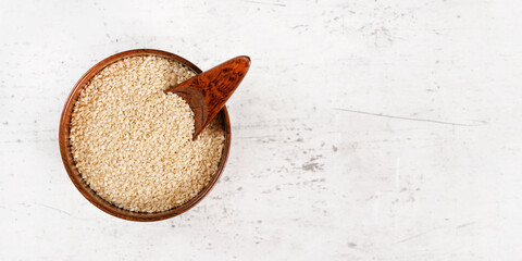 Wall Mural - White sesame - Sesamum indicum - seeds in small wooden cup on white stone like board, view from above