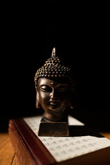 Poster - Vertical shot of a Buddha head statue placed on a book