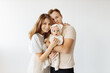 © shunevich - Portrait of a happy young family, with a little adorable daughter. Caring parents hold and gently hug their baby. Together they pose for a photo, looking at the camera. Family concept.