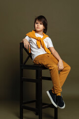 Handsome fashion young boy sits on a chair in studio on green background. Casual style. Stylish shooting in studio