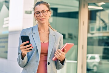 Young blonde businesswoman smiling happy using smartphone at the city.