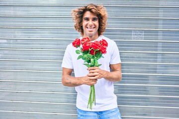 Wall Mural - Young handsome hispanic man smiling happy holding bouquet of roses standing  at street of city