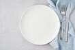 © Nata Bene - Clean empty white plate, fork and knife on pastel grey linen tablecloth on table, copy space, mock up, top view. Concept for menu with utensil
