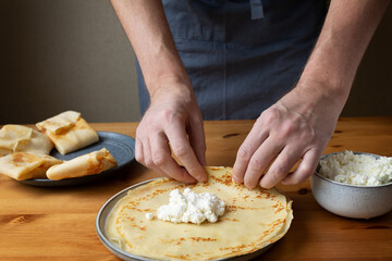 A man in the kitchen prepares a healthy breakfast of pancakes stuffed with fresh cottage cheese with sour cream and delicious fragrant honey.