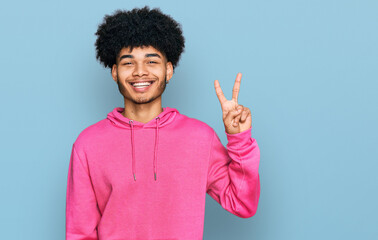 Young african american man with afro hair wearing casual pink sweatshirt showing and pointing up with fingers number two while smiling confident and happy.