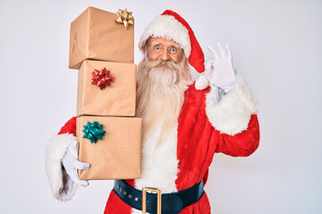 Wall Mural - Old senior man with grey hair and long beard wearing santa claus costume holding presents doing ok sign with fingers, smiling friendly gesturing excellent symbol