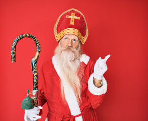 Wall Mural - Old senior man with grey hair and long beard wearing traditional saint nicholas costume pointing up looking sad and upset, indicating direction with fingers, unhappy and depressed.