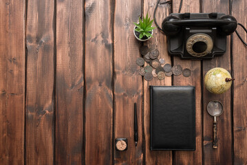 Wall Mural - Old coins, black rotary phone, leather book, magnifying glass, inkwell and quill pen on the brown wooden desk background with copy space.