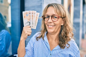 Middle age caucasian woman smiling happy holding uk pounds banknotes standing at the city.